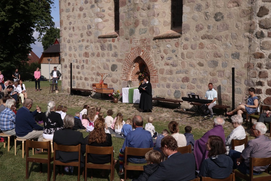 Sitzendes Publikum vor einer Kirchenwand die einem Programm mit Keyboardmusik und Andacht zuhören