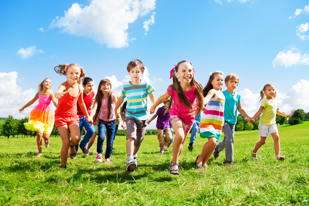 Etwa 10 bunt gekleidete Jungen und Mädchen rennen auf einer Wiese in eine Richtung und lachen